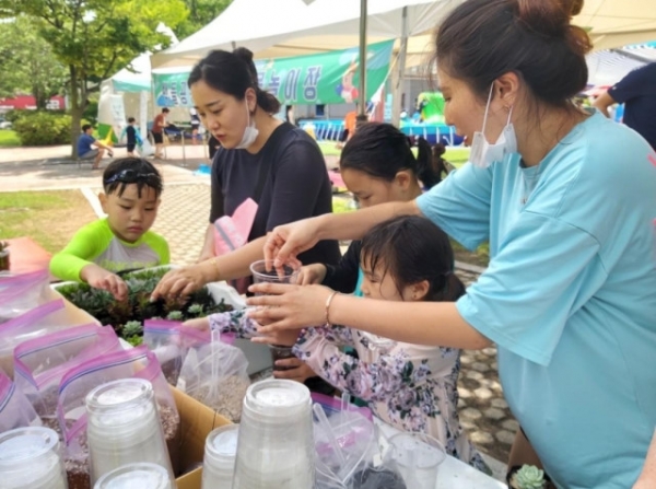 행사 참여자들이 직접 플라스틱 컵에 흙과 식물을 담아 화분을 만들고 있다.<br>